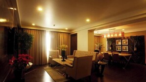 Un hall de hotel con sofá, sillas, zona de comedor y mostrador de recepción.