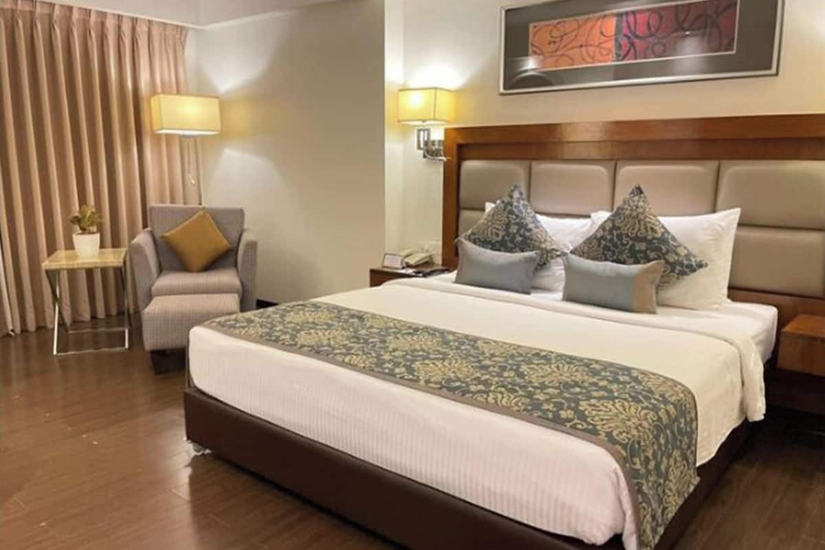 Quarto de hotel com uma cama grande, uma cadeira, uma mesinha de cabeceira e um abajur.