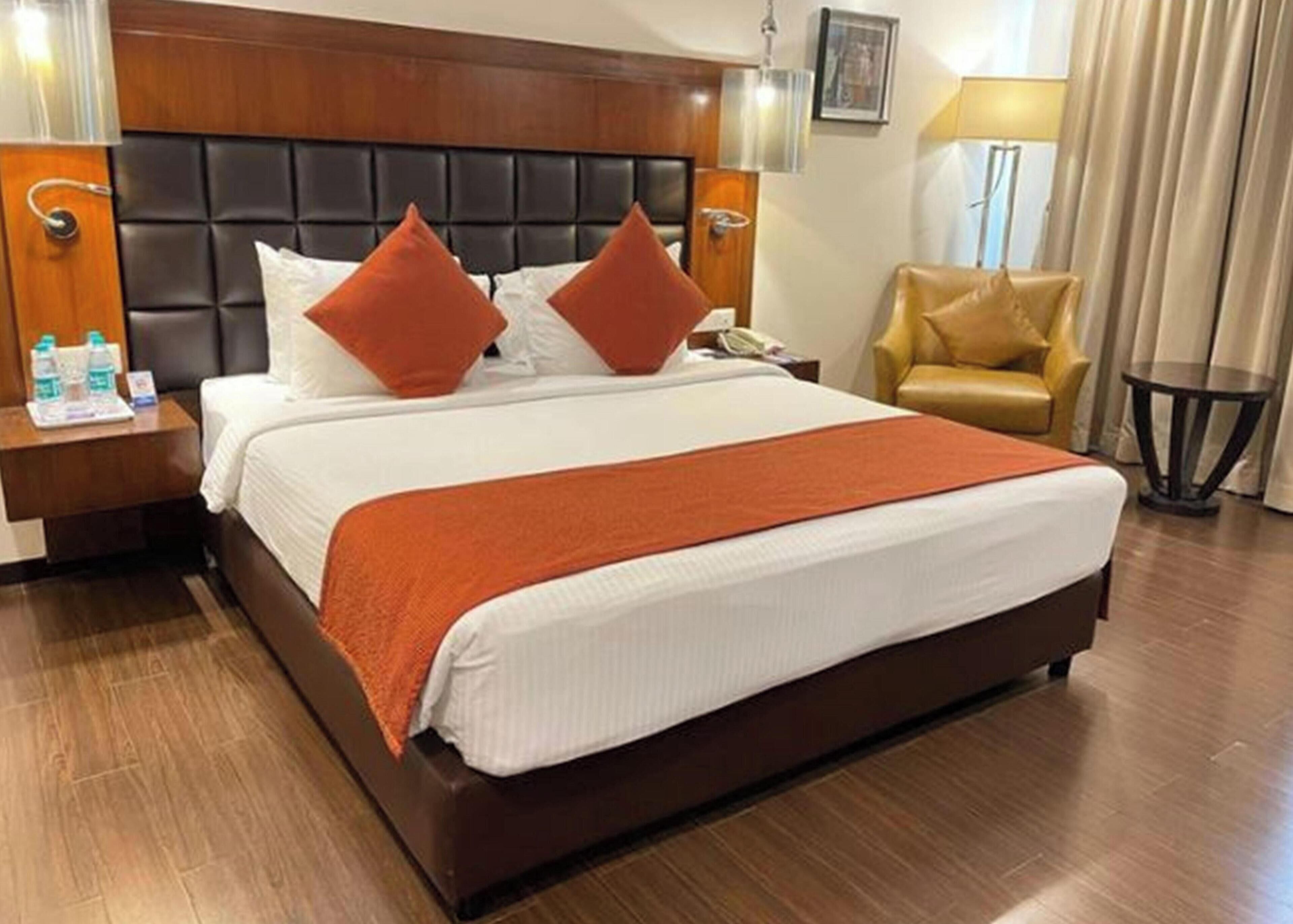 Une chambre d’hôtel avec un grand lit, une tête de lit en bois, deux tables de chevet, une chaise et une petite table.