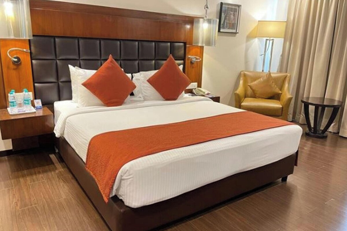 A hotel room with a large bed, wooden headboard, two nightstands, a chair, and a small table.