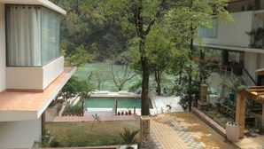 A modern building with a pool area, surrounded by greenery and trees. - Namami Ganges Resort (Narendranagar)