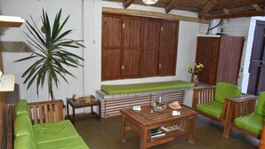 A cozy living room with a green sofa, wooden coffee table, and matching chairs. A large plant and a wooden cabinet are also visible.