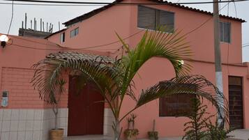 Un edificio rosa con puerta roja, plantas en macetas y un poste de electricidad.
