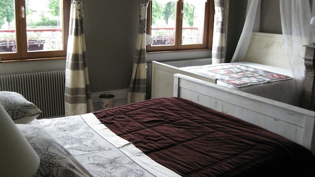 Een slaapkamer met een bed, een raam met gordijnen, een radiator en een klein tafeltje met een sprei.