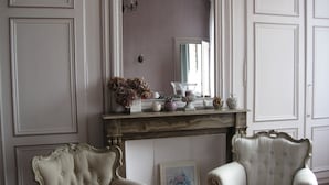 A room with two ornate armchairs, a fireplace mantel with decorative items, and a mirror reflecting the room. - Maison d'Hôtes Cap et Marais d'Opale (Saint-Omer)