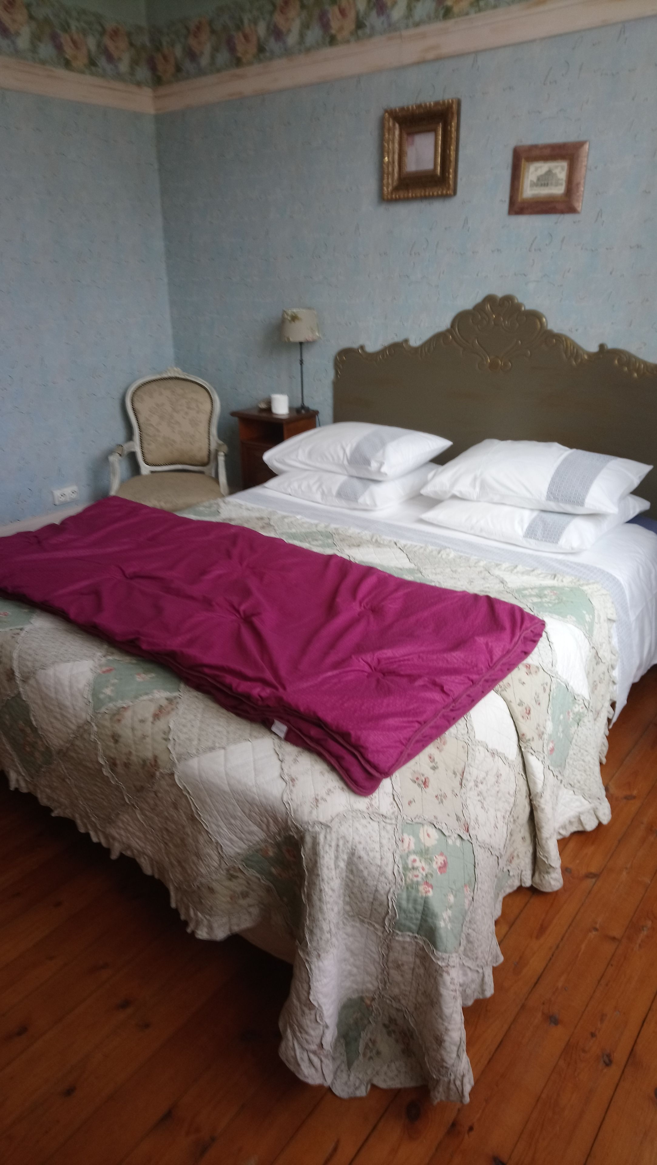 A bedroom with a bed, a chair, a nightstand, and a wall with framed pictures.