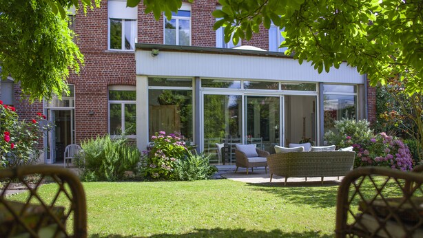 A modern house with a large glass door leading to a patio with outdoor furniture. - Maison d'Hôtes Cap et Marais d'Opale (Saint-Omer)