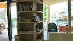 A living room with a curved bookshelf, a white sofa, and a view of the street through large windows. - Hotel Berenice Rimini Mare (Rimini)