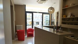 A modern kitchen with a central island, red chairs, and a view of the street through large windows. - Hotel Berenice Rimini Mare (Rimini)
