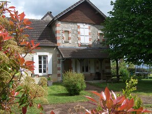 A two-story stone house with a sloped roof, a front porch, and a small garden area. - Gîte en Forterre (Druyes-les-Belles-Fontaines)