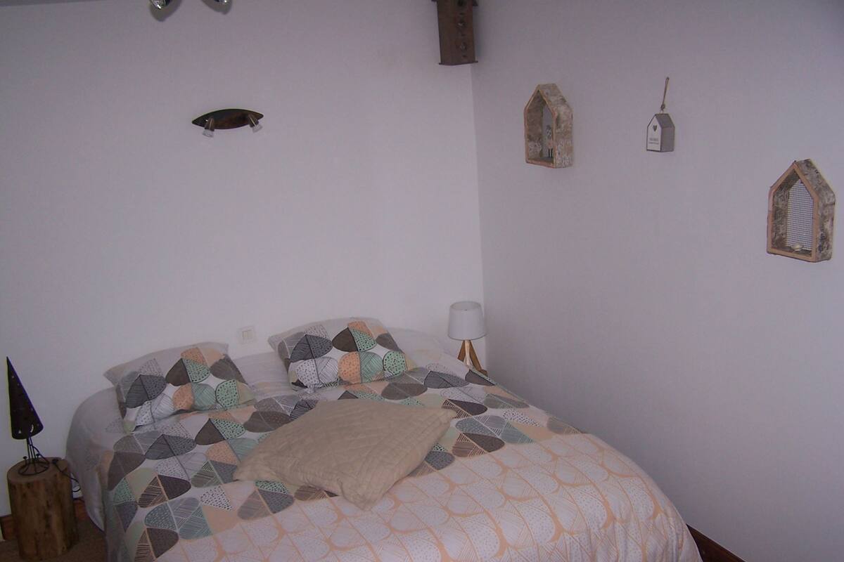 A bedroom with a bed, pillows, a lamp, and wall decorations including a fish, birdhouse, and a hanging ornament.