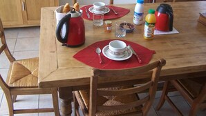 Et træspisebord dækket med en rød kedel, tepotte og sukker skål, samt en appelsinjuice og en termokande.