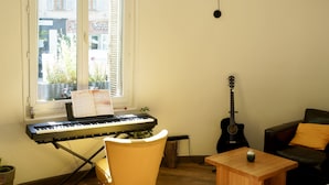 Une pièce avec un piano, une guitare, une table en bois et une chaise.