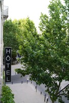 Une enseigne d’hôtel avec le mot « HÔTEL » et une vue sur une rue bordée d’arbres.
