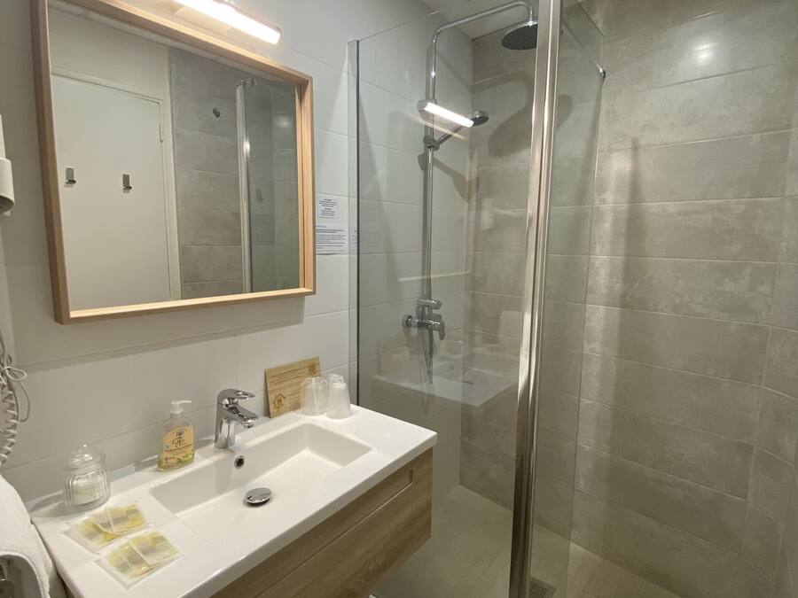 Een moderne badkamer met een douchecabine van glas, een wit wastafelmeubel met een houten kast, en een grote spiegel erboven.