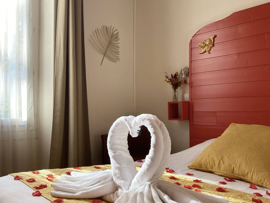 A hotel room with a bed, a red headboard, a decorative wall piece, and a window with curtains.