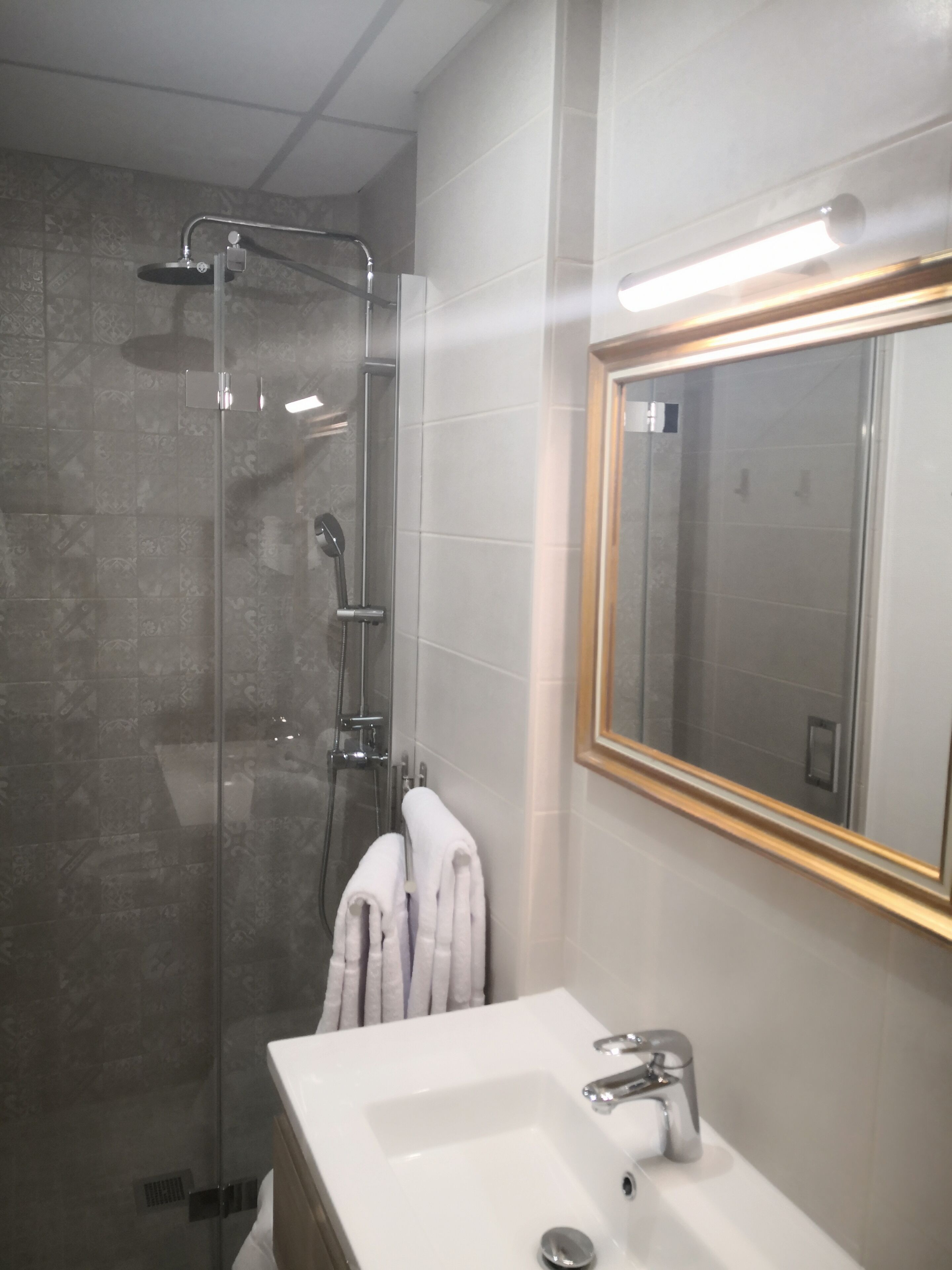 Un baño moderno con ducha envuelta en vidrio, un lavabo blanco y un espejo con marco dorado.