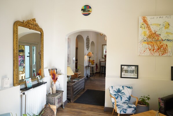 A spacious living area with a large mirror, a wooden floor, a blue and white chair, and a dining area in the background.