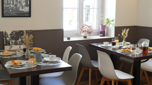 Un espace repas avec des tables préparées pour le petit-déjeuner, comprenant des croissants, des fruits et des boissons.
