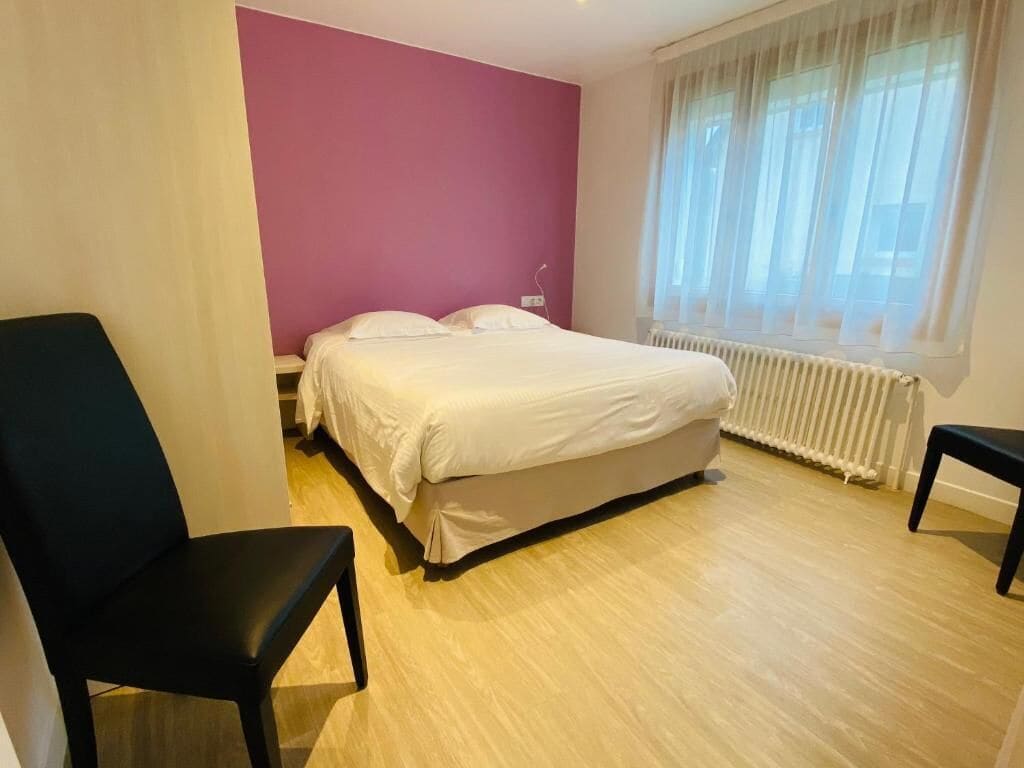 Een kamer met een bed, een stoel, een raam met gordijnen en een radiator.