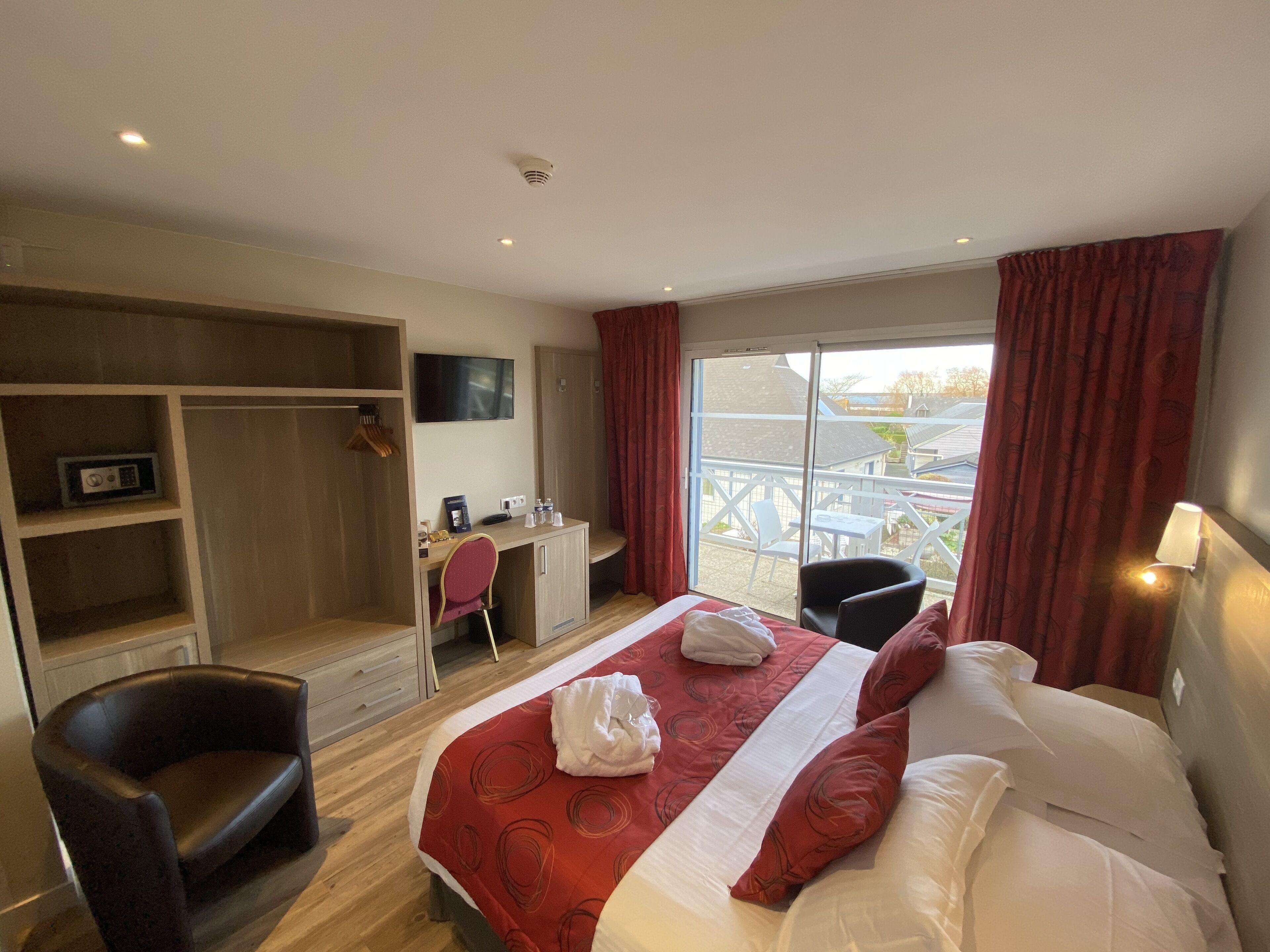 A hotel room with a bed, a desk, a chair, a wardrobe, and a window with a view of the outside.