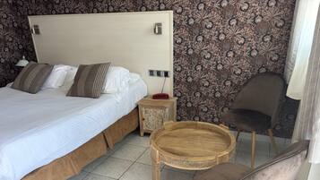 A neatly made bed with a wooden headboard, a bedside table with a lamp, a round wooden tray, and a chair.