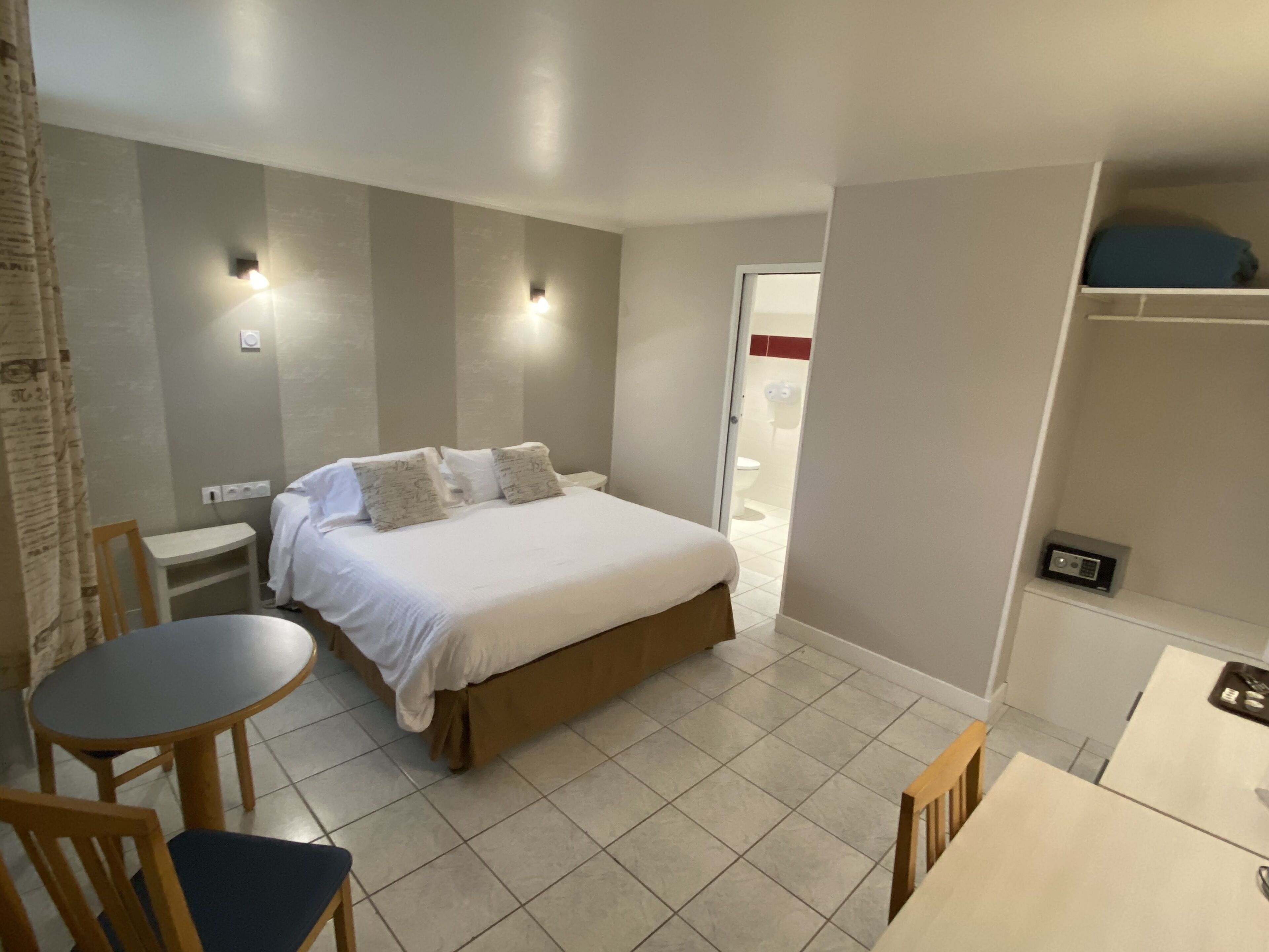 A hotel room with a bed, bedside tables, a chair, a small round table, and a wardrobe.