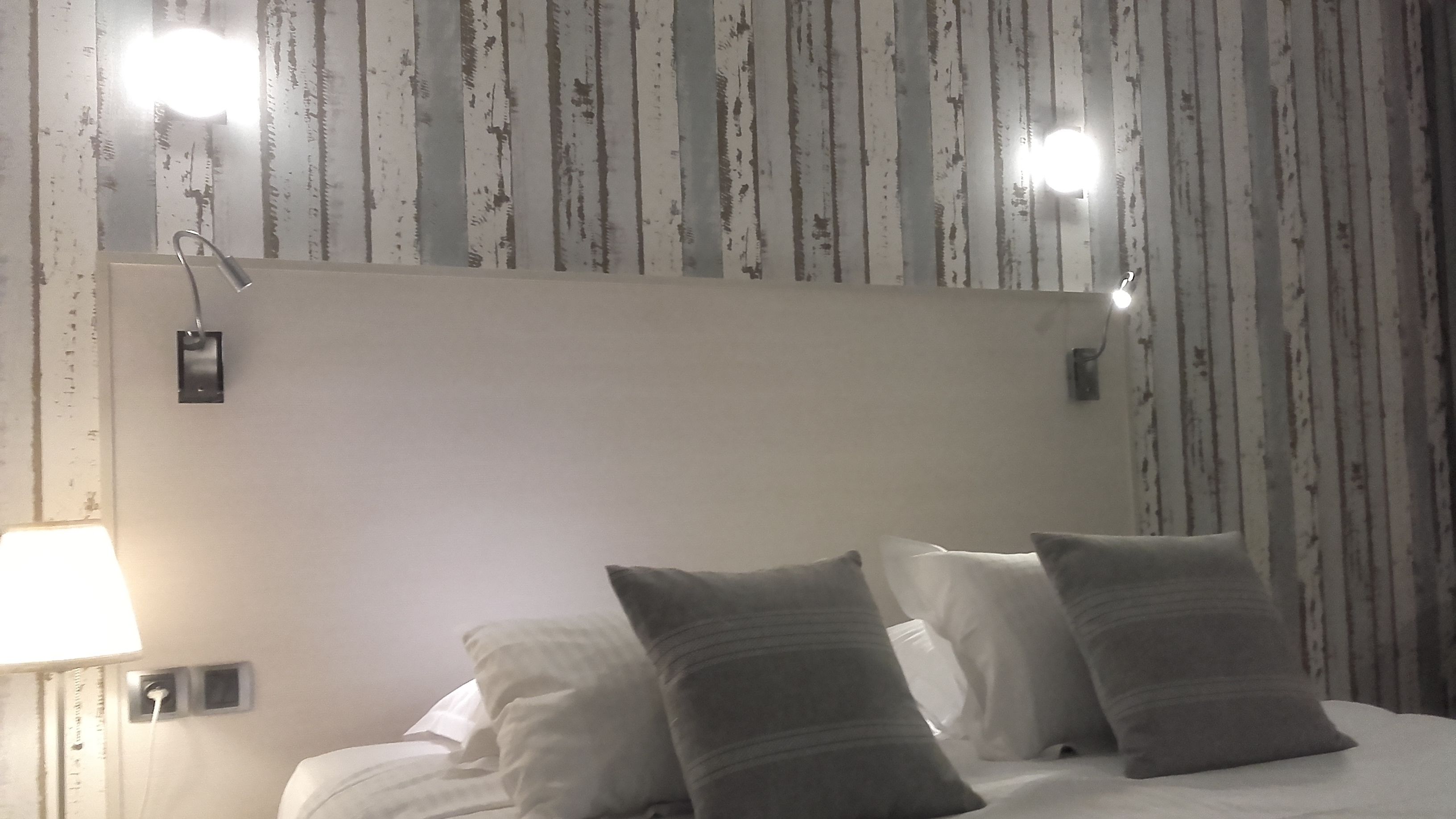 A hotel room with a large bed, two bedside lamps, and a mirror above the bed.
