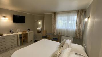 Habitación de hotel con cama, escritorio, silla, televisión y ventana con cortinas.