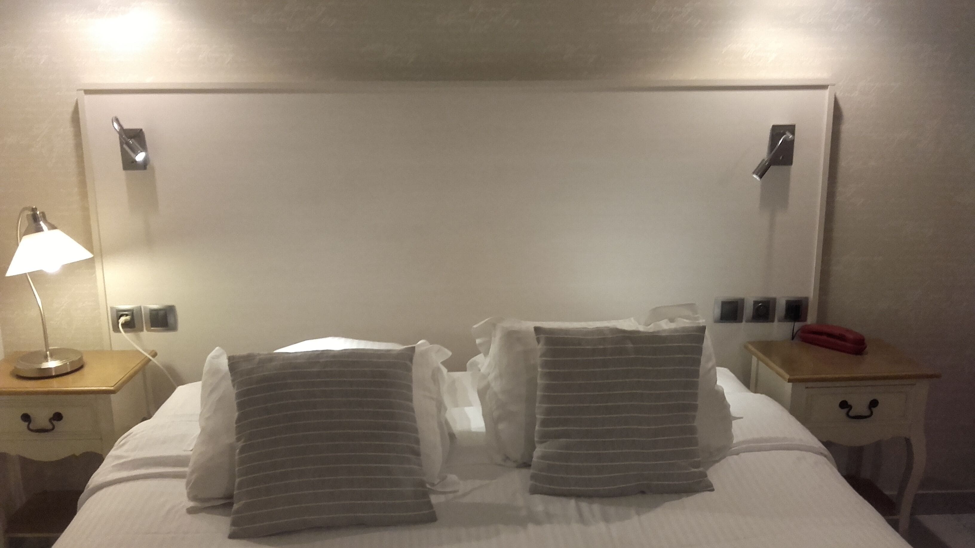 Habitación de hotel con una cama grande, dos mesitas de noche, una lámpara, un teléfono y un espejo en la pared.