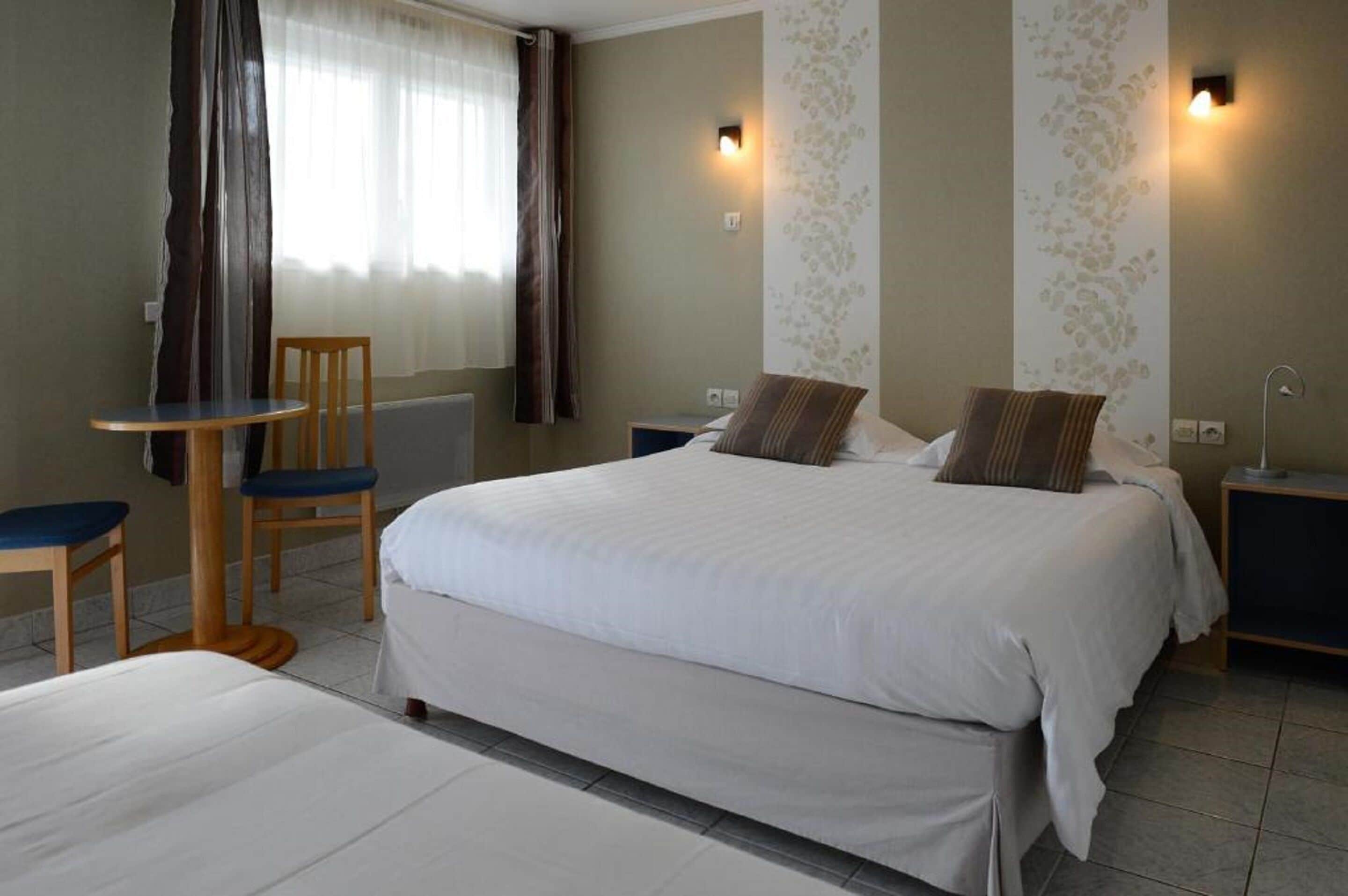 Habitación de hotel con una cama grande, una cama más pequeña, una silla, una mesa y dos mesitas de noche.