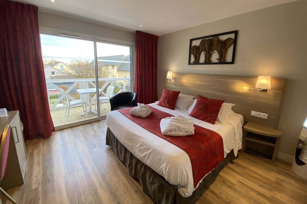 Ein Hotelzimmer mit einem großen Bett, einem Schreibtisch, einem Stuhl und einem Balkon mit Blick auf Häuser.