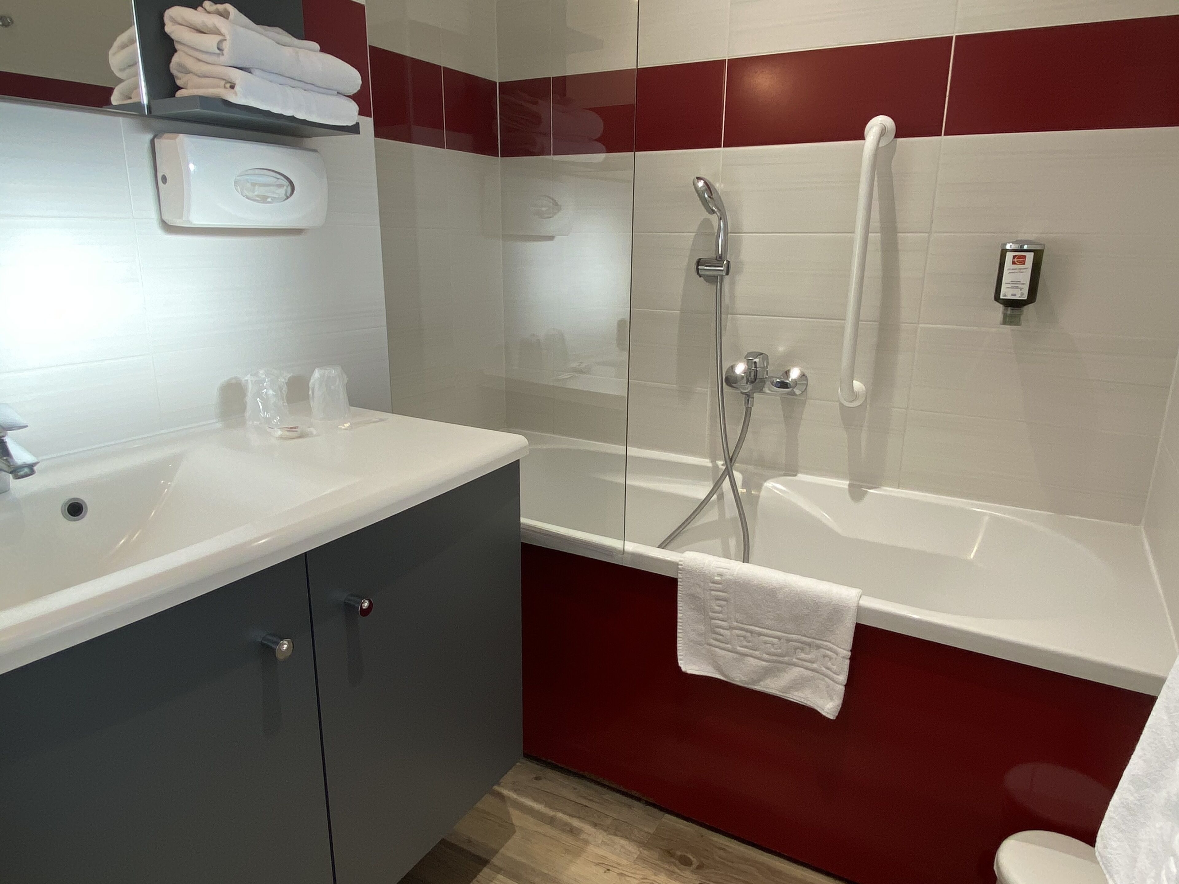 Een moderne badkamer met een witte wastafel, een douche met glazen wanden en rode en witte betegelde muren.
