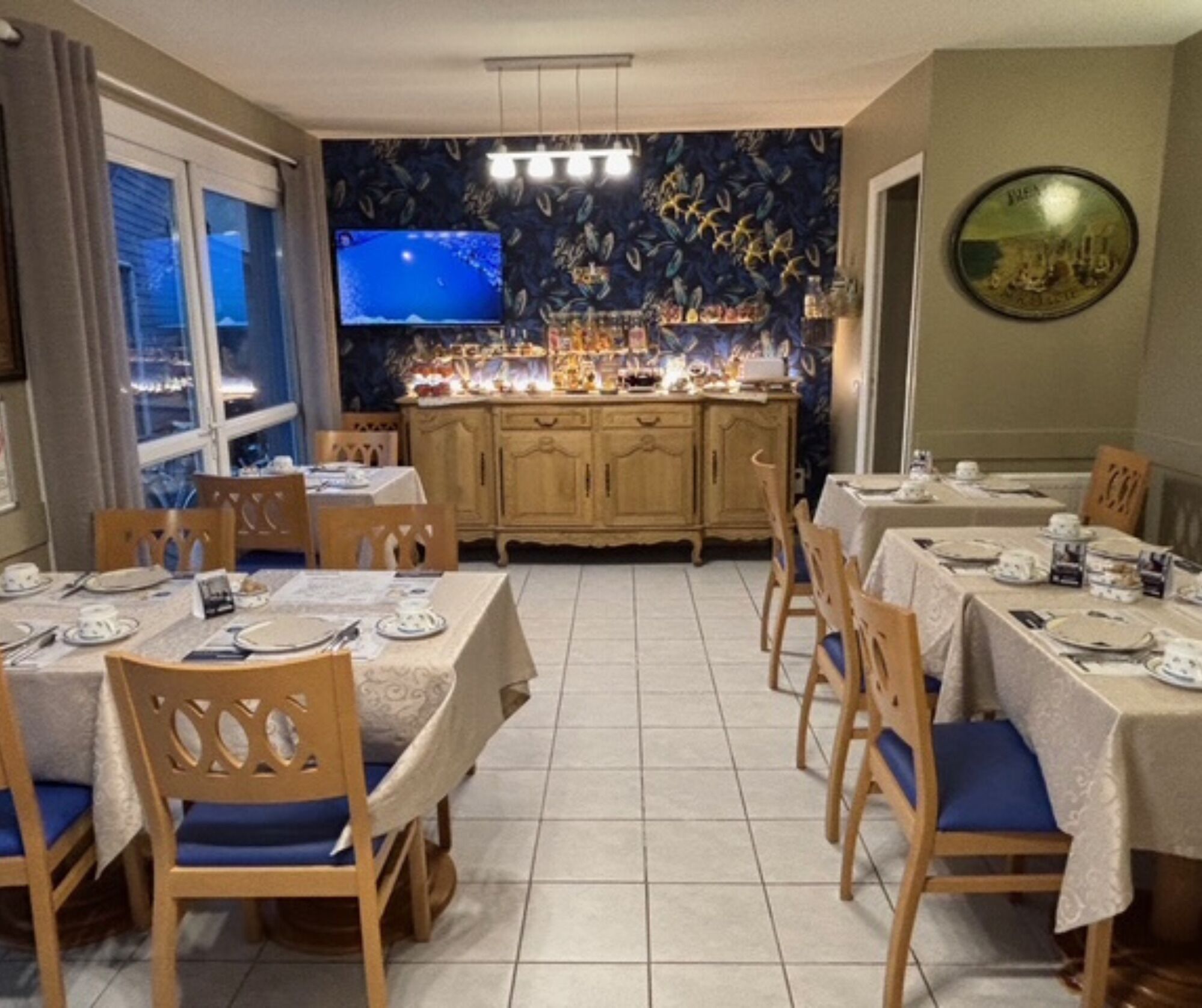 Un comedor con mesas dispuestas para cuatro, sillas de madera, un televisor en la pared y un mural decorativo.