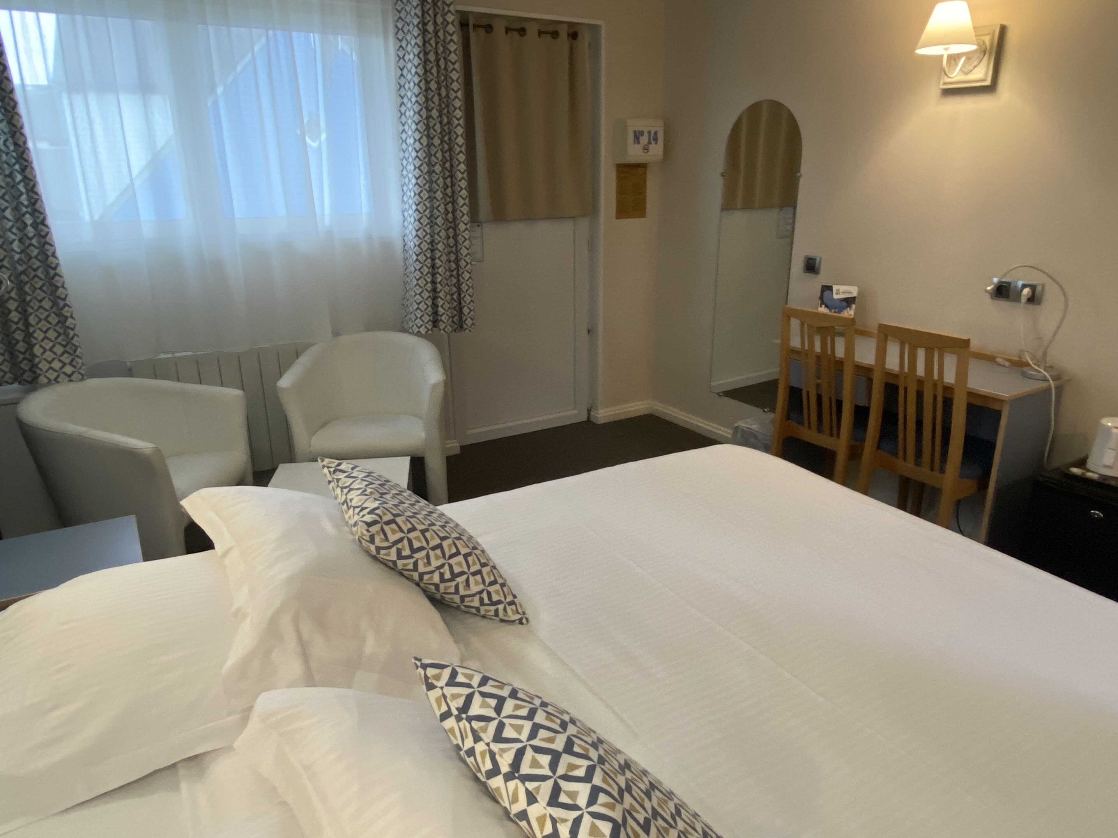 A hotel room with a large bed, two chairs, a desk, and a mirror.