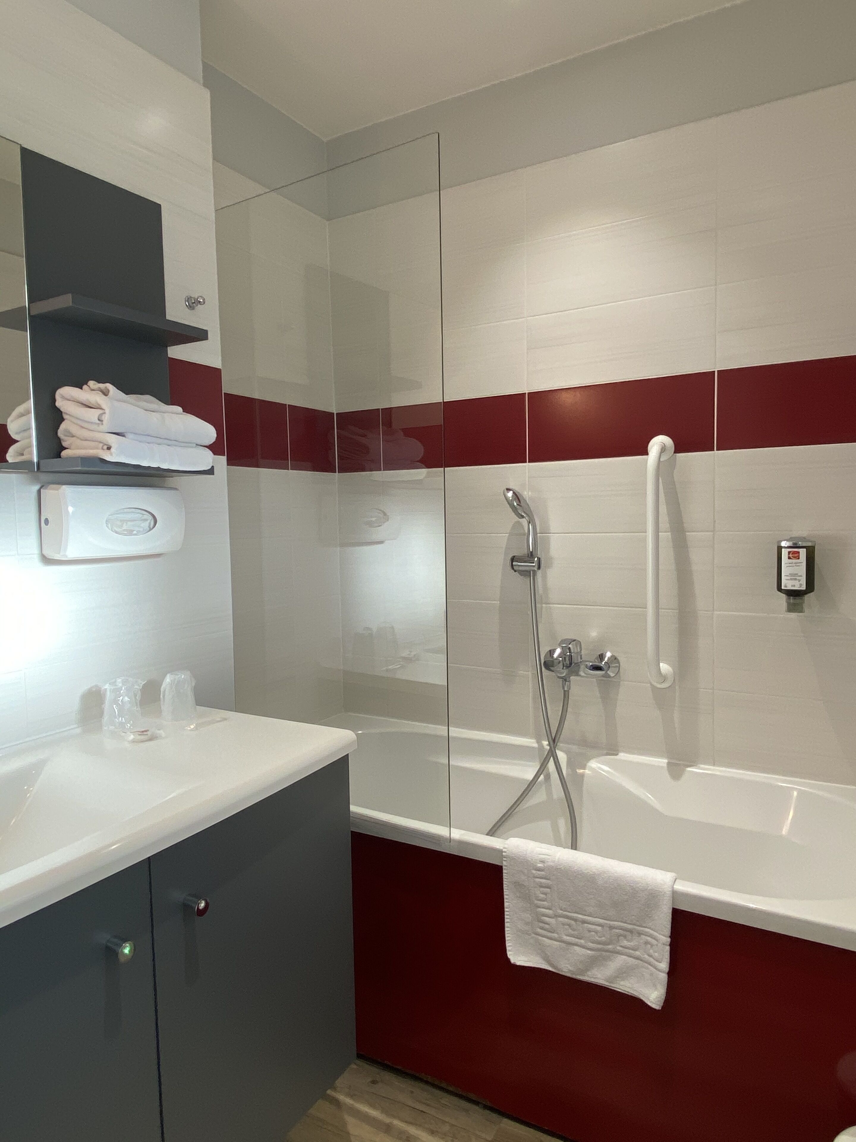 A modern bathroom with a glass-enclosed shower, a white bathtub, and a vanity with a towel rack.
