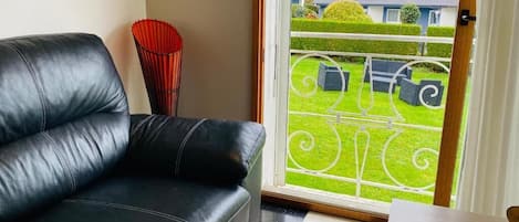Een woonkamer met een zwarte leren bank, een rode vaas, en uitzicht op een groen gazon en huizen door een glazen deur.