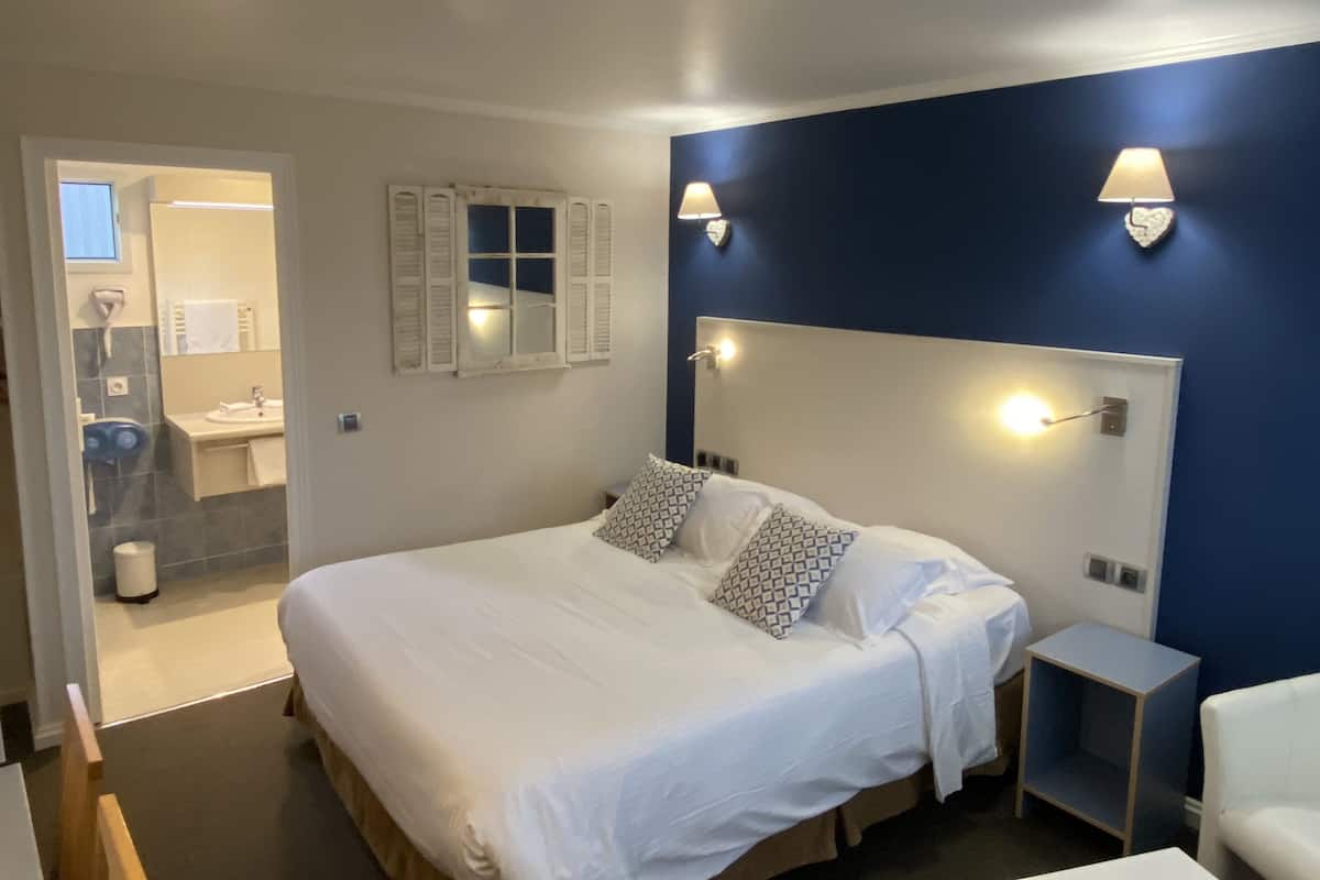 Ein Hotelzimmer mit einem großen Bett, Nachttischen, einem Schminktisch und einem Fenster mit Rollläden.