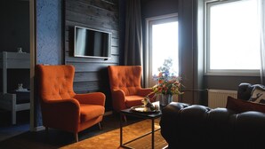 Un salón con dos sillones naranjas, una mesa de centro, una chimenea y un televisor montado en la pared.