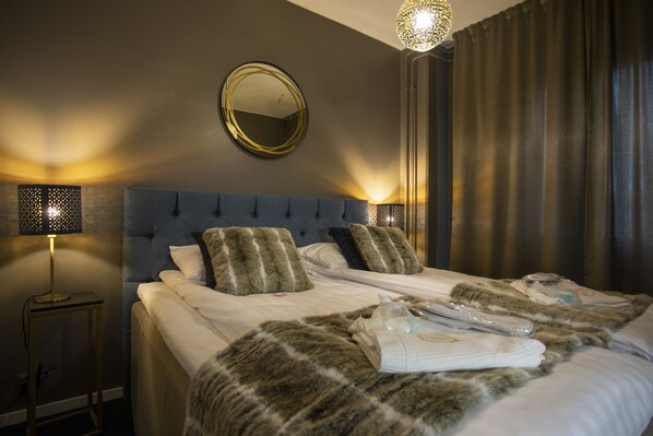 A neatly made bed with a fluffy blanket, a round mirror on the wall, and a lamp on the nightstand.