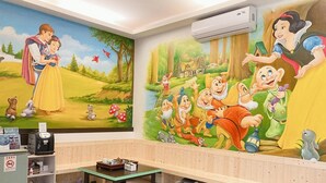 A children's room with a mural of Disney characters, a wooden bench, a table with items, and a small piggy bank.