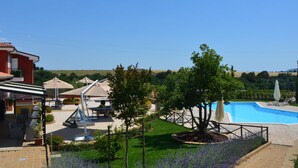 A pool area with a clear view of the surrounding landscape, including a red building and a grassy lawn. - Il Podere di Marfisa (Farnese)