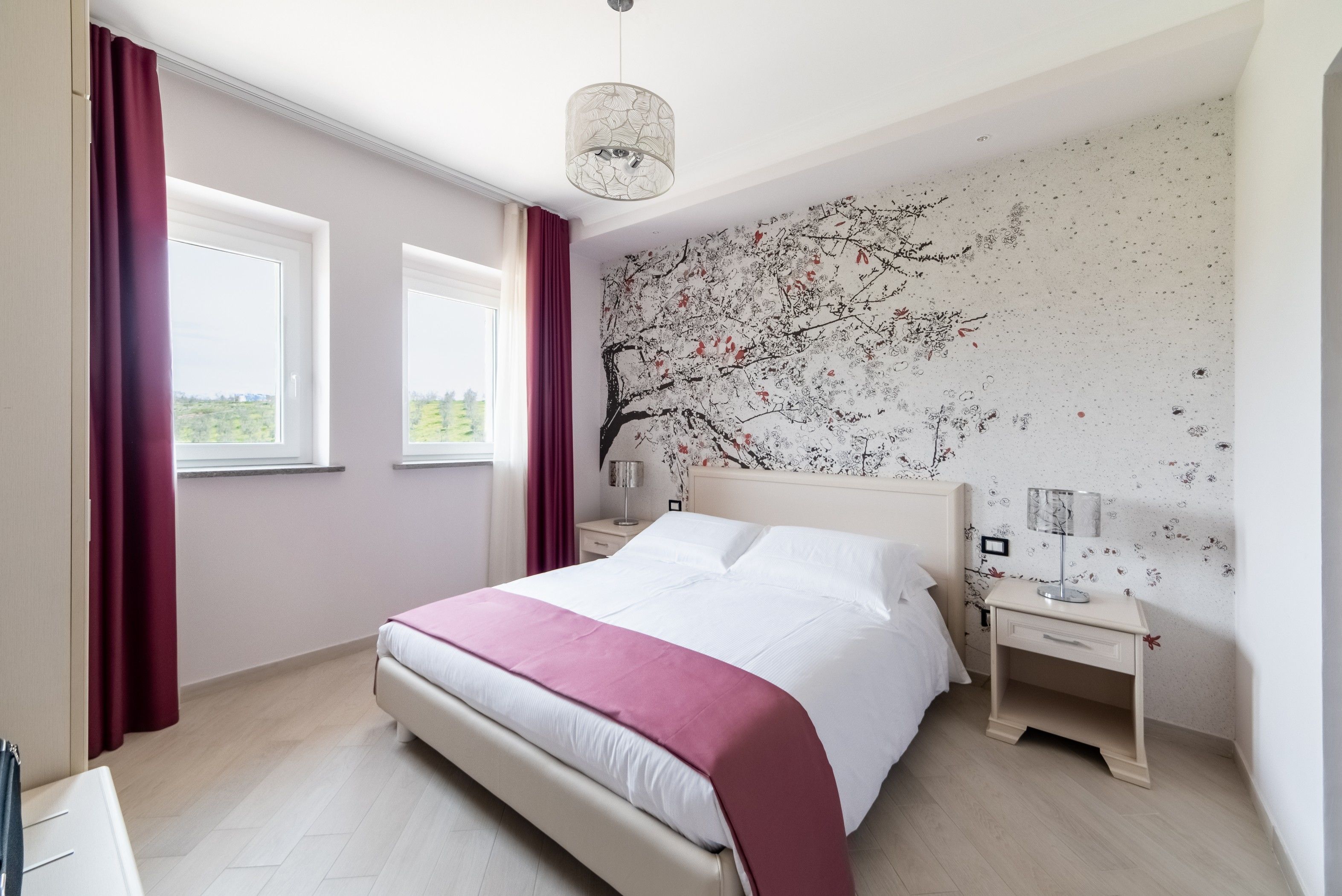A modern bedroom with a large bed, a nightstand, a lamp, and a wall mural.