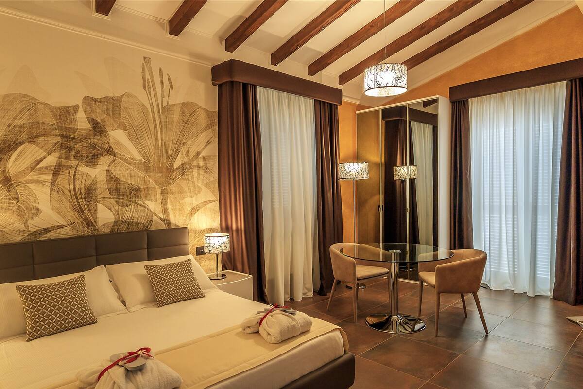 A hotel room with a bed, a desk, a chair, and a large abstract painting on the wall.