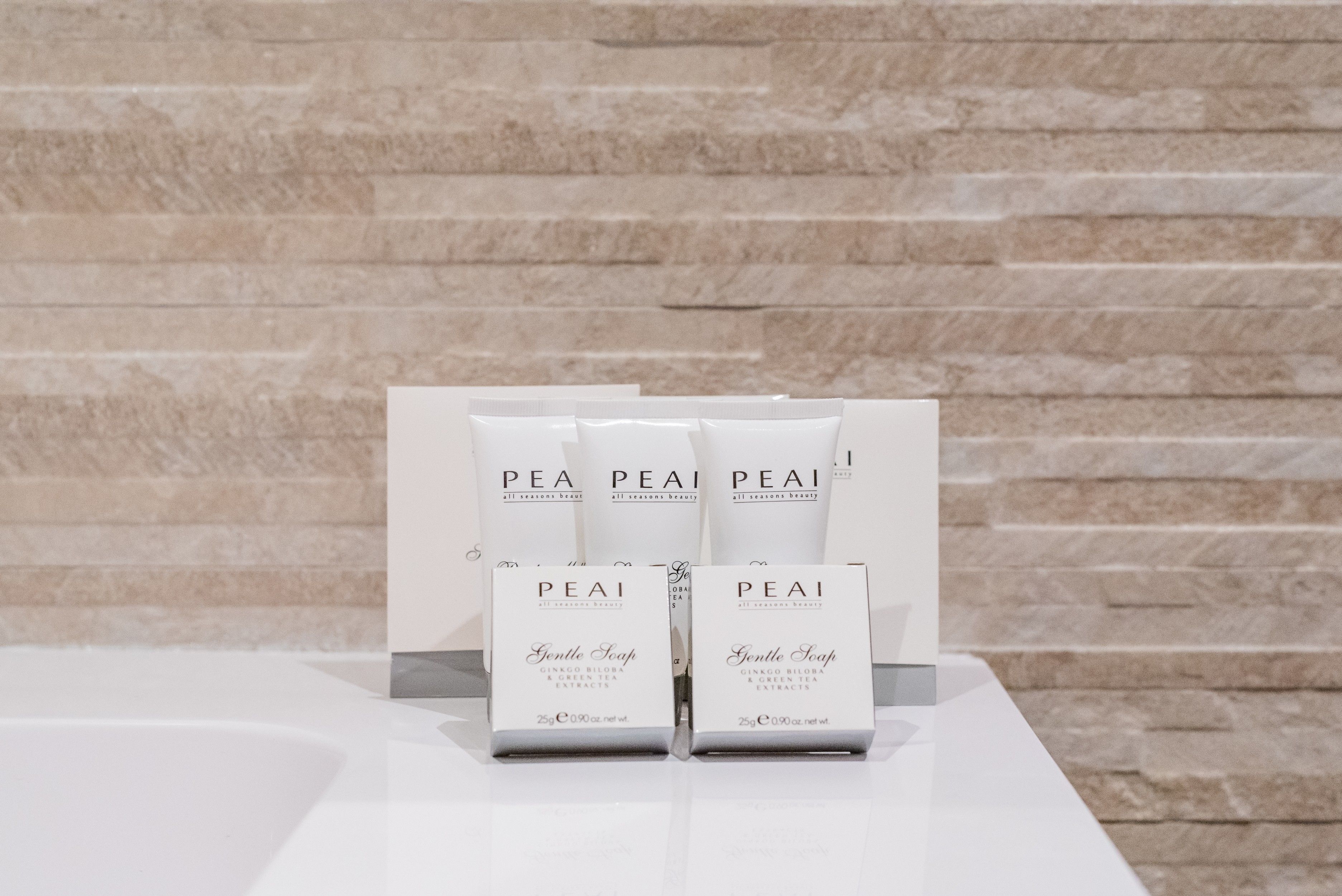 Three packages of PEAI Gentle Soap on a white surface against a stone wall background.
