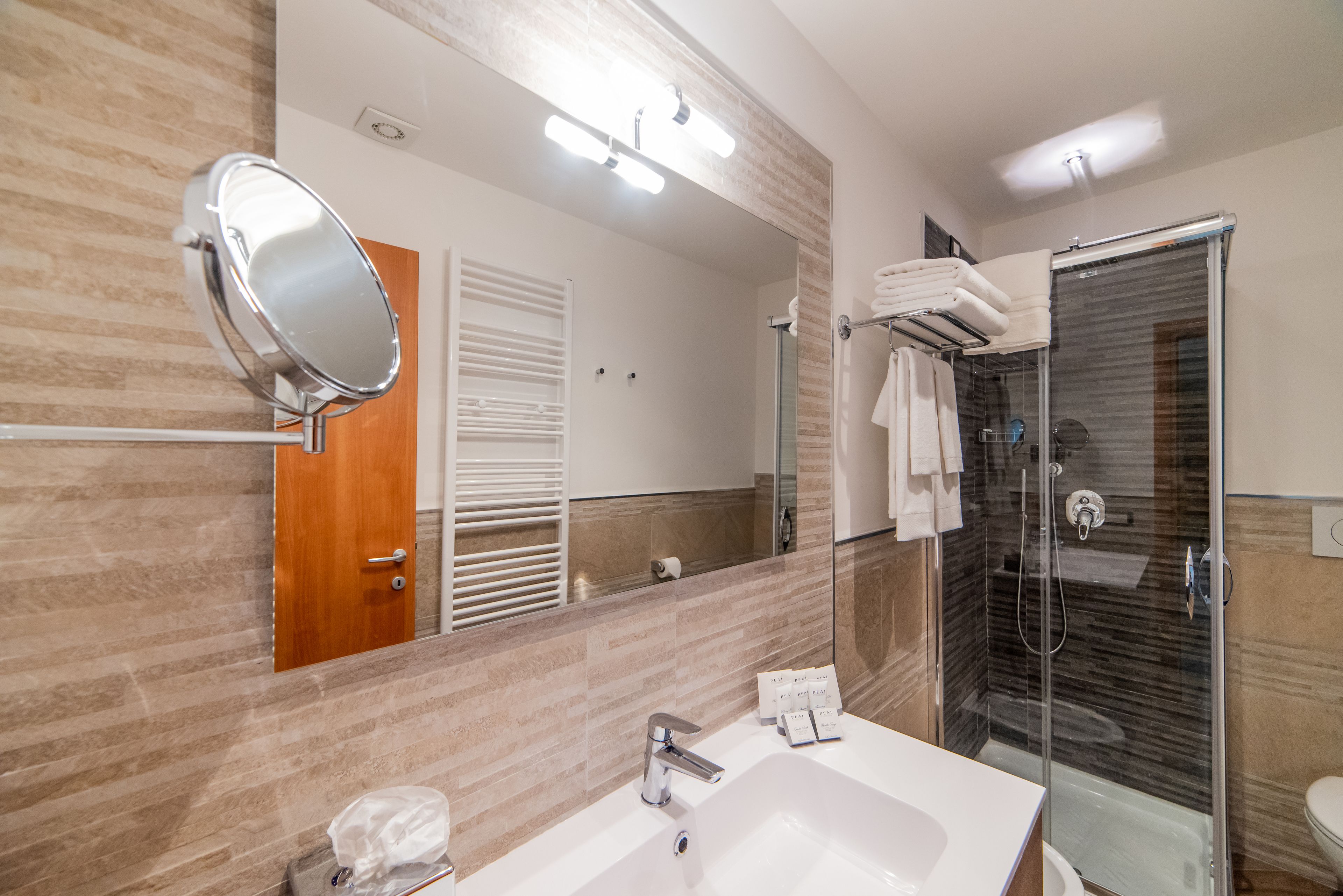 A modern bathroom with a large mirror, a sink, and a glass-enclosed shower.