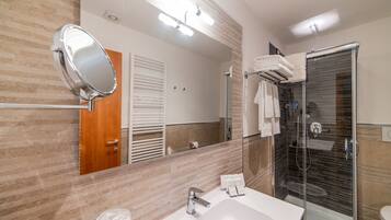 A modern bathroom with a large mirror, a sink, and a glass-enclosed shower.