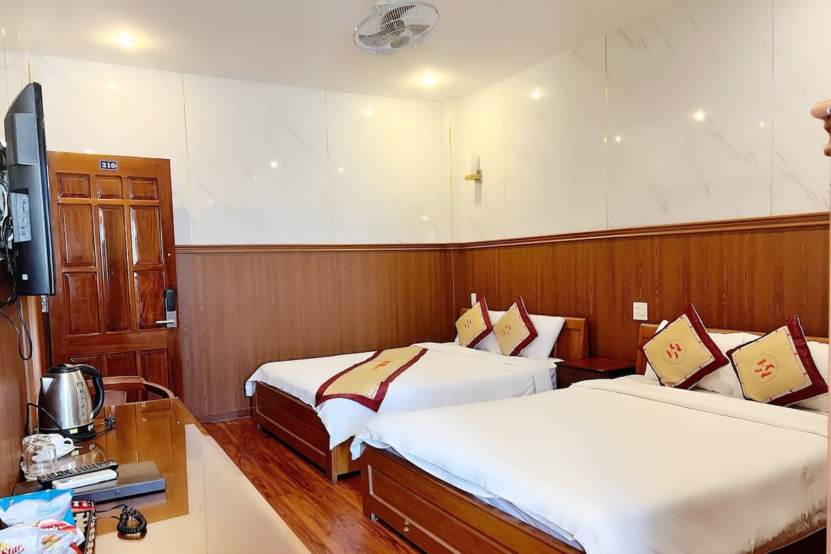 Une chambre d’hôtel avec deux lits, des têtes de lit en bois, un bureau en bois avec une bouilloire, une télévision et un minibar.