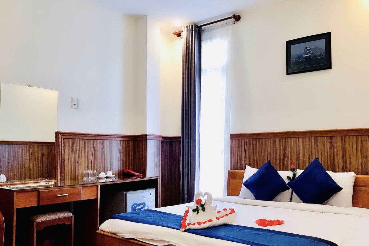 Une chambre d’hôtel avec un bureau en bois, un lit avec une literie bleue et blanche, et un tableau accroché au mur.