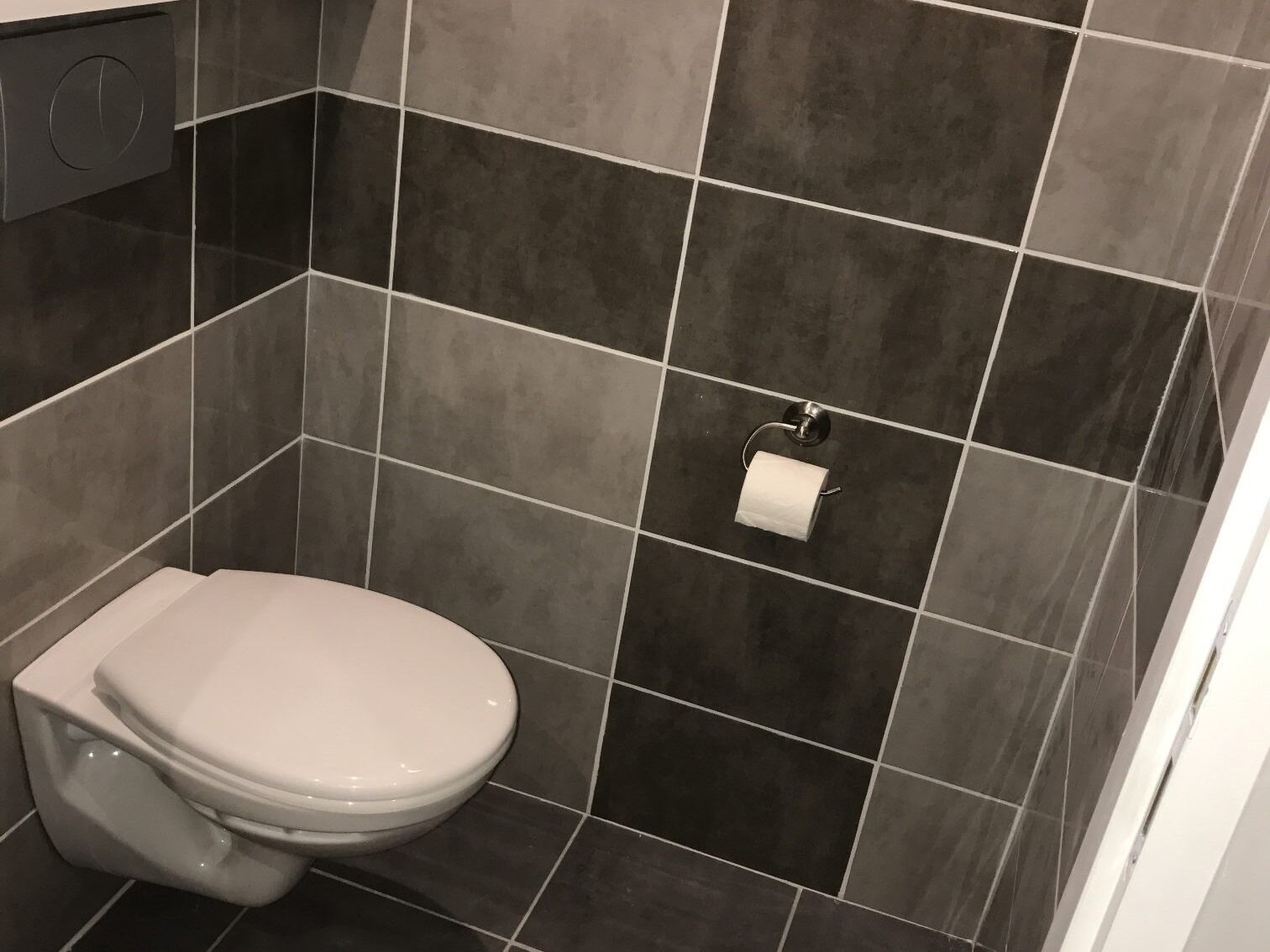 Een badkamer met toilet, donkere betegelde wanden en een toiletrolhouder.